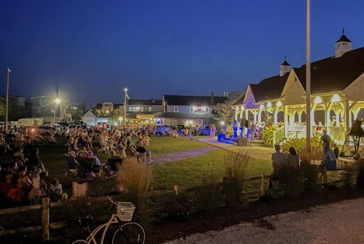 Exterior view of a recreation area surrounded by a large green lawn full of people enjoying a concert at dusk