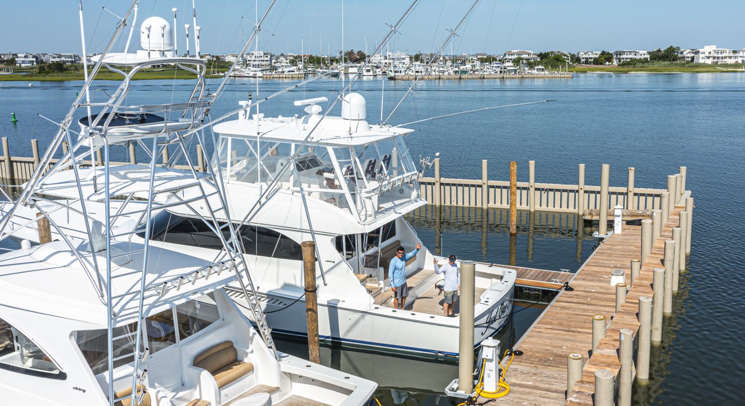 Two large white boats in the harbor with two people standing on a boat waving