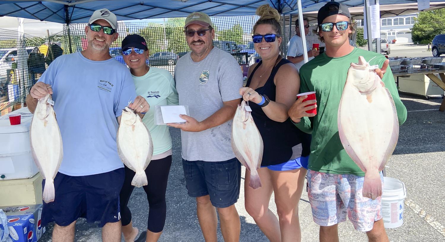 Group of people standing and holding large white round fish that they caught fishing