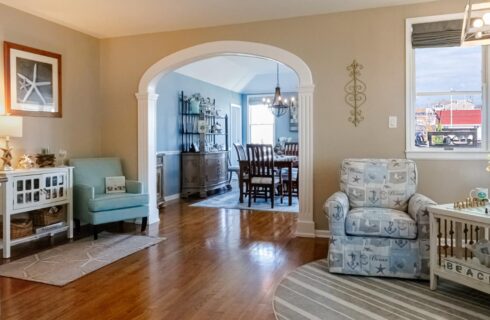 Dining room with light colored walls, hardwood flooring, wooden trim, large dining table, wooden chairs, and view to living room