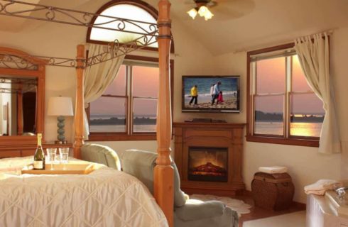 Bedroom with light colored walls, hardwood flooring, wooden trim, wooden four-poster bed, fireplace, and view of the ocean