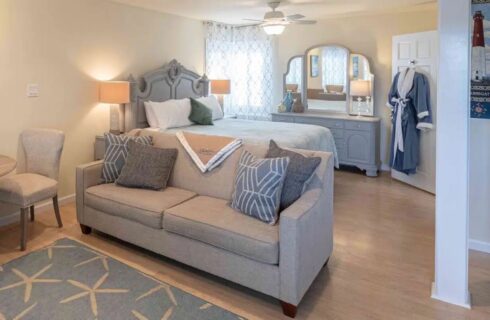 Bedroom with light cream walls, hardwood flooring, gray wooden headboard and dresser, light tan upholstered sofa, and sitting area