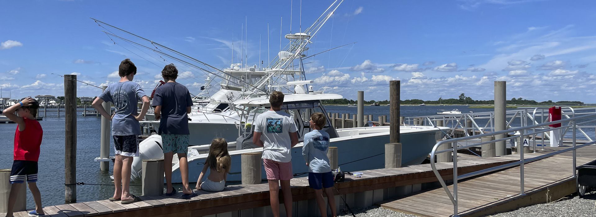Handful of kids standing on a dock looking at boats in the harbor